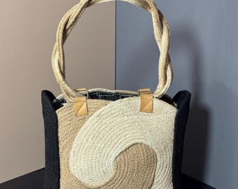 May include: A woven tote bag with a spiral design in beige, tan, and black. The bag has a twisted rope handle and leather accents. The bag is made of natural fibers and has a rectangular shape.