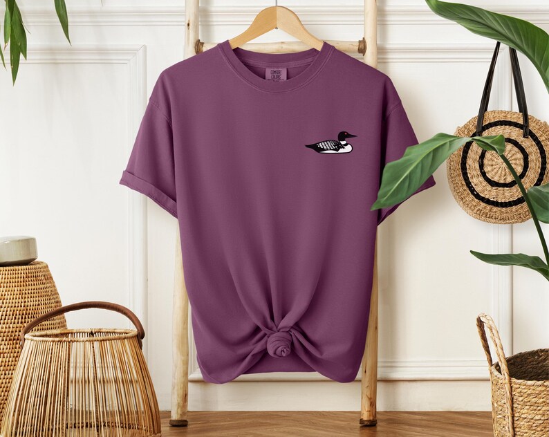 May include: A purple short-sleeved t-shirt with a black and white loon graphic on the front.