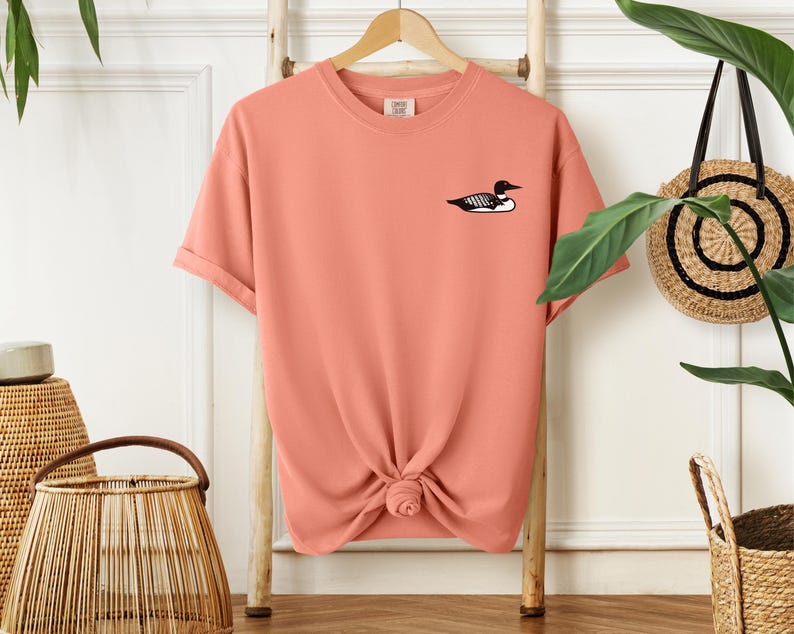May include: A coral coloured t-shirt with a black and white loon graphic on the front.