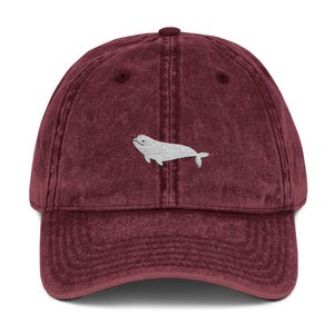 May include: A maroon vintage washed cotton baseball cap with a white embroidered beluga whale design.