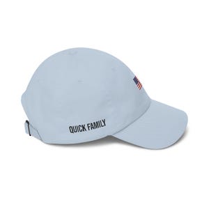 Puede incluir: Gorra de b&eacute;isbol azul claro con visera curva. La gorra tiene el texto "QUICK FAMILY" en negro en el lateral y un peque&ntilde;o parche de la bandera americana. Correa ajustable en la parte trasera.