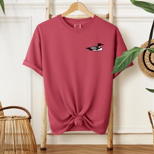 May include: A pink t-shirt with a black and white loon graphic on the front.