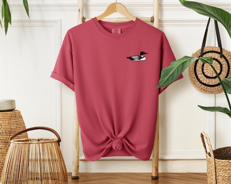 May include: A pink t-shirt with a black and white loon graphic on the front.
