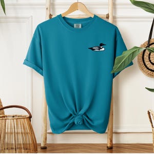 May include: A teal blue t-shirt with a black and white loon graphic on the front.