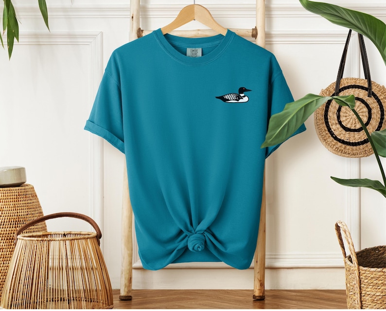 May include: A teal blue t-shirt with a black and white loon graphic on the front.