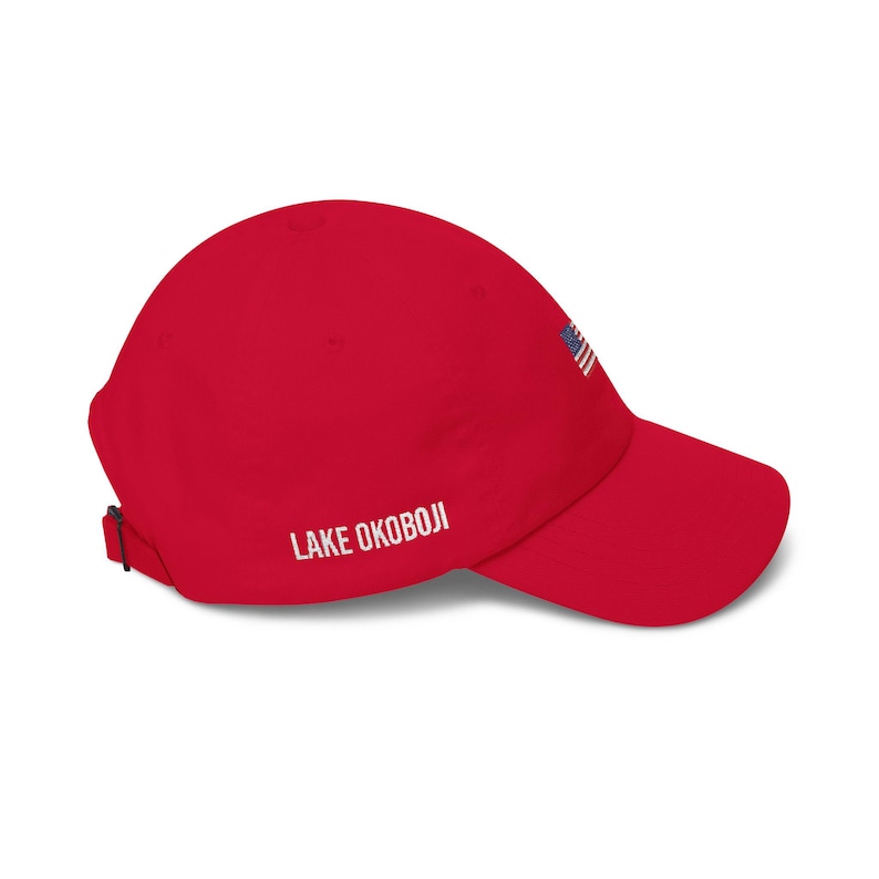Puede incluir: Gorra de b&eacute;isbol roja con visera curva. La gorra tiene el texto "LAKE OKOBOJI" en blanco en el lateral y un peque&ntilde;o dise&ntilde;o de la bandera estadounidense. Tiene una correa ajustable en la parte trasera.