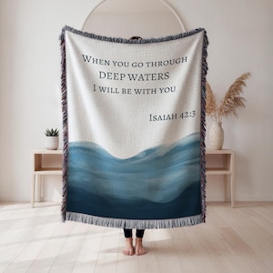 Könnte beinhalten: Eine gewebte Decke mit dem Text "WHEN YOU GO THROUGH DEEP WATERS I WILL BE WITH YOU ISAIAH 42:3". Das Design zeigt eine blaue Welle im Aquarellstil am unteren Rand und einen cremefarbenen Hintergrund.