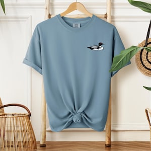 May include: A light blue t-shirt with a black and white loon graphic on the left chest.