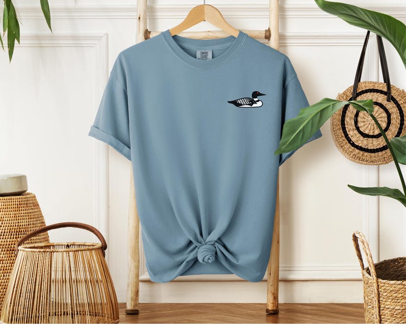 May include: A light blue t-shirt with a black and white loon graphic on the left chest.