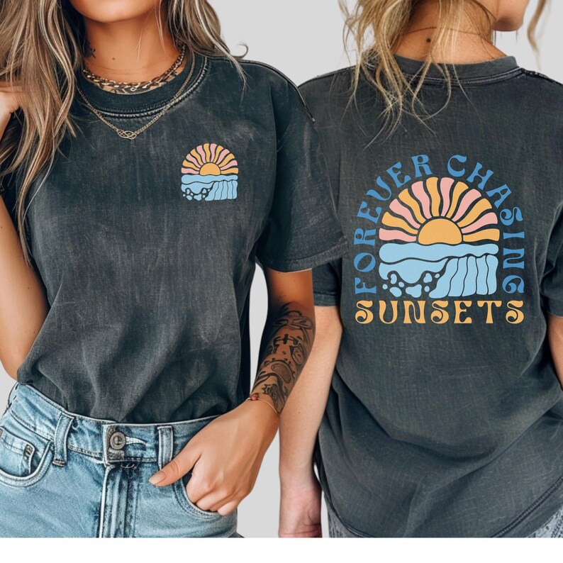 May include: Dark gray t-shirts with a sunset graphic. The front of the shirt has a small sunset design. The back of the shirt has the words "Forever Chasing Sunsets" around a larger sunset graphic. The shirts are worn by two people.