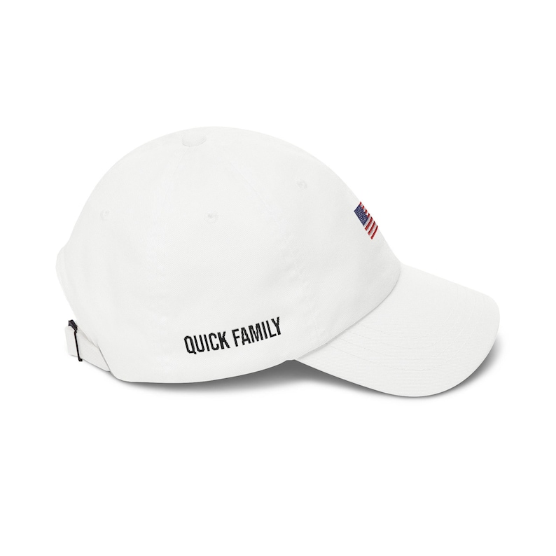 Puede incluir: Gorra de b&eacute;isbol blanca con visera curva. Presenta una peque&ntilde;a bandera americana bordada y el texto "QUICK FAMILY" en negro. La correa ajustable es visible en la parte trasera.