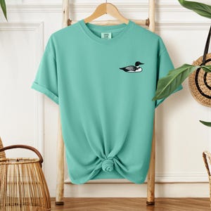 May include: A turquoise blue t-shirt with a black and white loon graphic on the front.