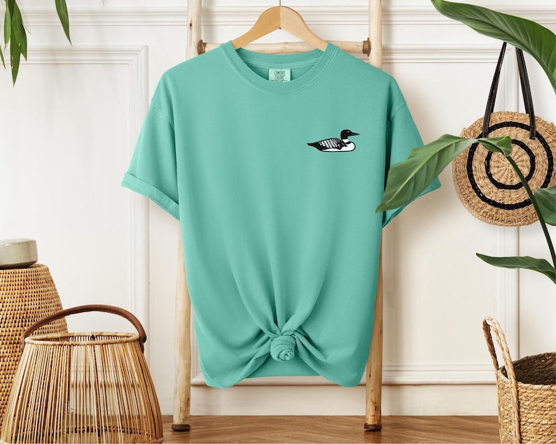 May include: A turquoise blue t-shirt with a black and white loon graphic on the front.
