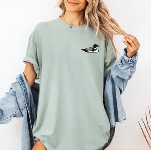 May include: A light green t-shirt with a black and white loon graphic on the front.