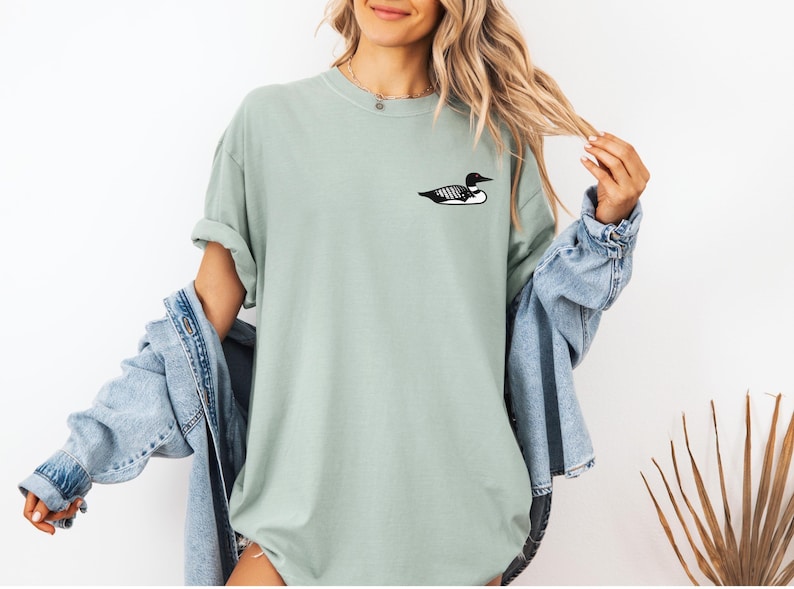May include: A light green t-shirt with a black and white loon graphic on the front.