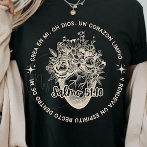 Puede incluir: Camiseta negra con un diseño floral dentro de un marco circular. El diseño incluye el texto "CREA EN MI, OH DIOS, UN CORAZON LIMPIO, Y RENUEVA UN ESPIRITU RECTO DENTRO DE MI. Salmo 51.10". El arreglo floral tiene forma de jarrón.