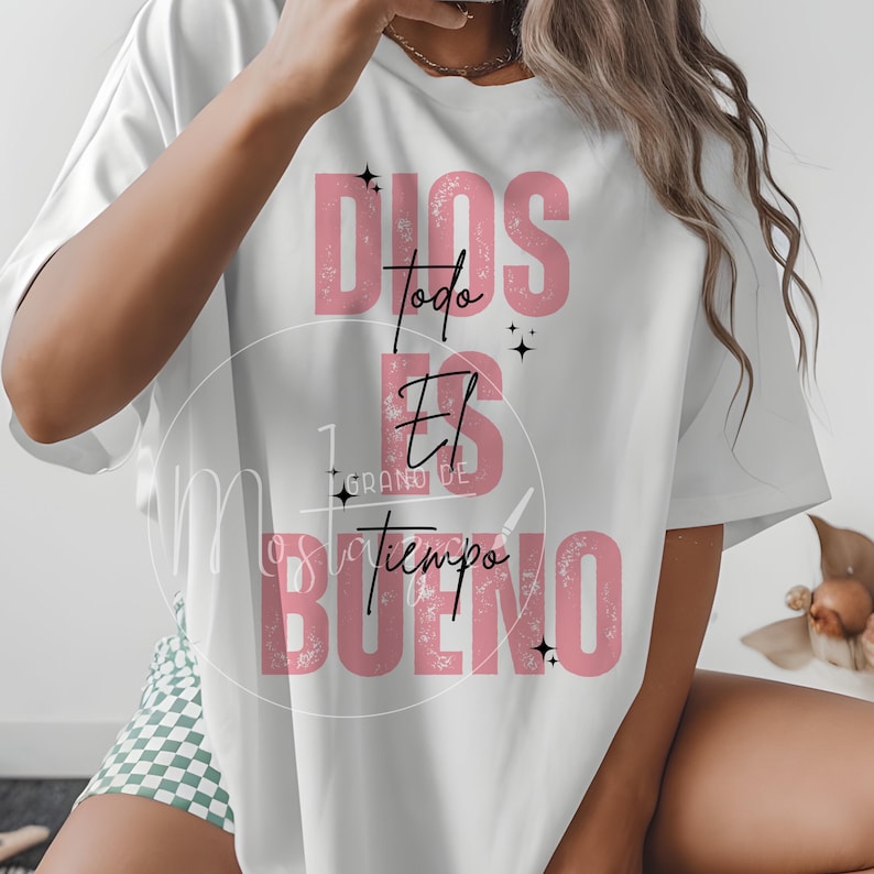 May include: White t-shirt with the text "Dios es el tiempo bueno" in pink. The text is arranged vertically with the words "Dios", "todo", "El", "tiempo", and "Bueno" in a stylized font. Small black star graphics are included.