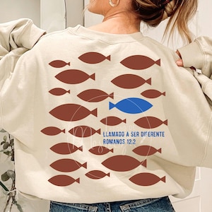 Könnte beinhalten: Beiges Sweatshirt mit braunem Fischmuster und einem blauen Fisch. Der Text "LLAMADO A SER DIFERENTE ROMANOS 12:2" ist blau gedruckt. Das Sweatshirt ist aus weichem Material.