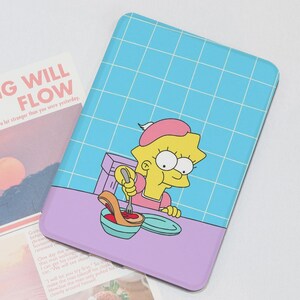 May include: A rectangular case featuring a cartoon character, Lisa Simpson, in a cooking scene. The case has a blue grid background, a purple base, and the text "RYTHING WILL FLOW" on a nearby paper.