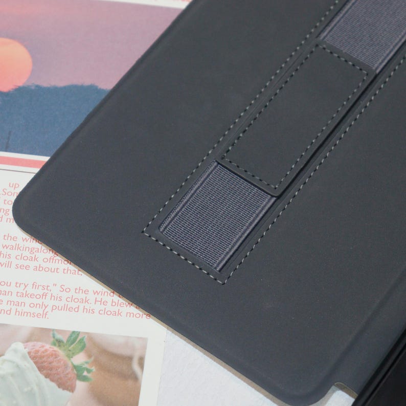 K&ouml;nnte beinhalten: Schwarze Lederh&uuml;lle mit zwei Gummib&auml;ndern zum Halten eines Tablets oder E-Readers.