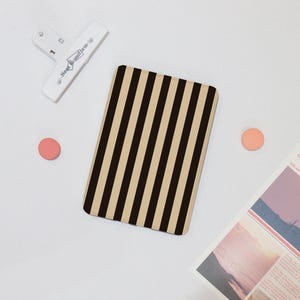 May include: A black and beige striped e-reader cover. The cover is made of a soft, durable material and has a sleek, modern design.