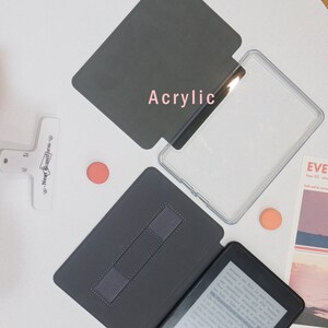 K&ouml;nnte beinhalten: Zwei verschiedene H&uuml;llen f&uuml;r einen E-Reader. Eine H&uuml;lle ist aus klarem Acryl und die andere ist eine schwarze, lederartige H&uuml;lle mit einem eingebauten St&auml;nder.