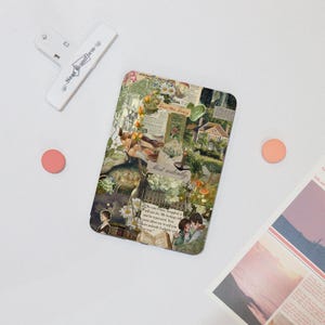 May include: A rectangular decorative magnet with a collage design featuring floral and literary elements, including text that reads "Most ardently." A white clip and two pink circles are also present.