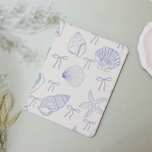 May include: A white notebook cover with a blue seashell and starfish pattern. The pattern also includes blue bows.