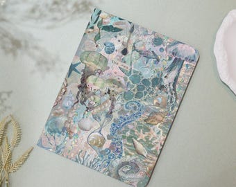 May include: A light blue notebook with a watercolor design of sea creatures, shells, and seaweed. The text "the sea" is printed on the cover.