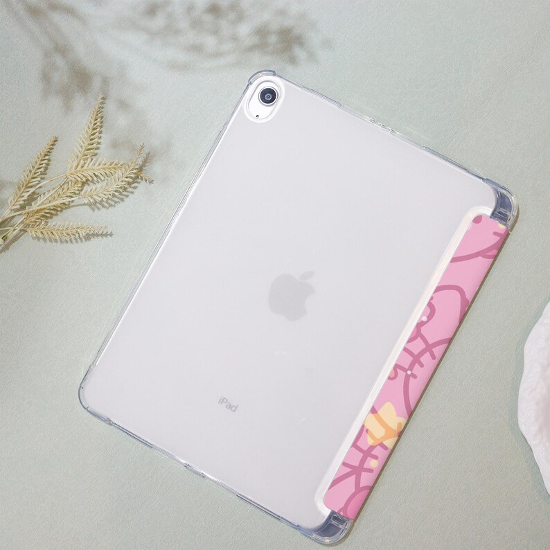May include: A clear plastic case for an iPad with a pink and yellow patterned design on the back. The case has a cutout for the camera lens and the Apple logo is visible on the back.