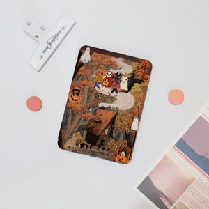 May include: A rectangular Halloween-themed illustration featuring a haunted house, a winding road, and various cartoon characters in costumes. The color palette includes orange, brown, and white. A white clip with the text "Near Uniform" is in the upper left corner.