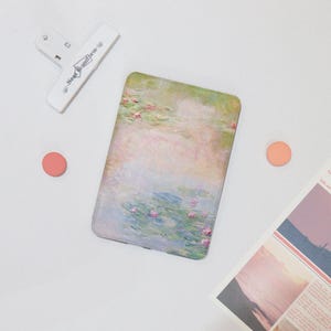 May include: A close-up of a white e-reader with a colorful painting of water lilies on the cover. The painting is in a soft, impressionistic style with shades of blue, green, pink, and white.