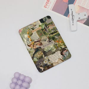 May include: A rectangular decorative item with a collage design featuring floral elements, vintage text, and illustrations. The text "Most ardently" is visible. The item is surrounded by other objects, including a white clip and a cluster of purple spheres.