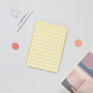 May include: A notebook with a yellow and white gingham pattern is on a white surface, alongside a white clip with the text "Near Uniform". Two small, round, orange stickers and a piece of paper with a picture are also present.