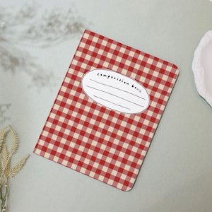 Op de afbeelding: Rood-wit geruit schriftboek met een blanco label waarop "composition book" staat.