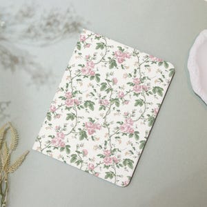 May include: A floral notebook featuring a pattern of pink roses and green leaves on a white background. The notebook has rounded corners and a soft, vintage aesthetic. The design is reminiscent of classic floral wallpaper.