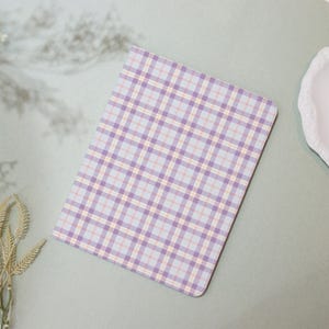 Può includere: Un taccuino rettangolare con un motivo a quadri pastello nei toni del lavanda, azzurro e pesca. Il taccuino è appoggiato su una superficie verde chiaro, con un elemento decorativo bianco sullo sfondo.