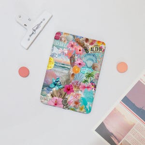 May include: A rectangular, colorful phone case with a collage of beach-themed images, including seashells, flowers, and the word "Aloha." The case is surrounded by a white clip, a pink circle, and a newspaper clipping.