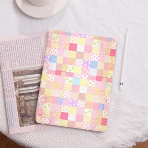 Könnte beinhalten: Eine iPad-Hülle mit einem rosafarbenen und gelben Patchwork-Muster und einem weißen Stift.