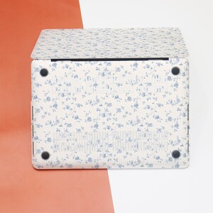 May include: A white laptop case with a blue floral pattern. The case has a smooth, matte finish and is designed to fit a standard laptop.
