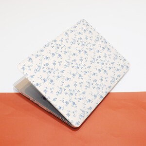 May include: A white laptop case with a blue floral pattern. The case is closed and the laptop is visible inside.