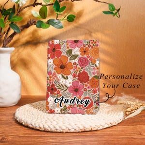 May include: A floral phone case with a beige background and a pattern of orange, pink, and red flowers. The name "Audrey" is written in cursive. Text on the case reads "Personalize Your Case."