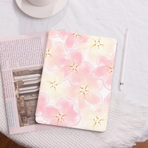 Op de afbeelding: Een roze en witte iPad-hoes met een bloemenpatroon in aquarel-stijl. De hoes heeft een herhalend patroon van delicate roze en witte bloemen met een subtiele gouden omtrek.