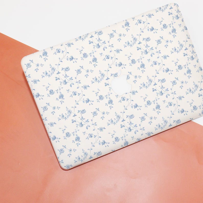 May include: A white laptop cover with a blue floral pattern. The cover has a cutout for the Apple logo.