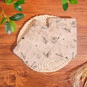 May include: Two rectangular wooden boards featuring a light wood grain finish and black line art illustrations of world maps, airplanes, hearts, planets, and stamps. The text "and so the adventure begins" is printed on both boards.