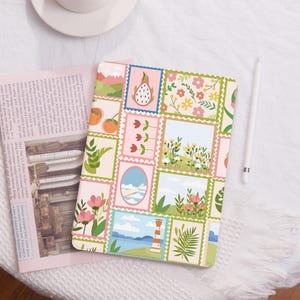 May include: A pink and green patterned iPad case featuring a variety of images including flowers, fruit, and a lighthouse. The case has a vintage postage stamp design.