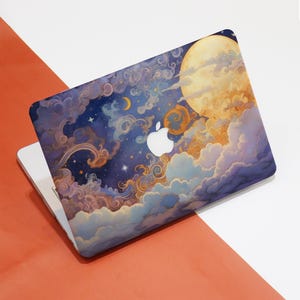 Op de afbeelding: Een laptop met een kleurrijk, artistiek ontwerp met een nachtelijke hemel met een volle maan, wolken, sterren en een halve maan. Het ontwerp is overwegend blauw, goud en wit. Het Apple-logo is zichtbaar.