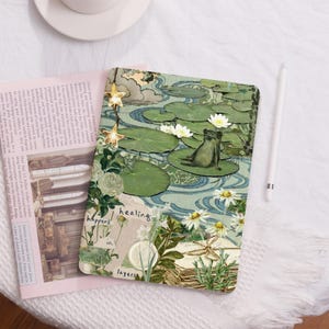 May include: A green frog sits on a lily pad in a pond with white flowers. The background is a collage of green leaves, blue water, and white flowers. The text "healing happens in layers" is written on the bottom of the image.