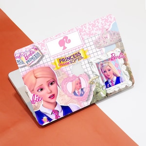 Pode incluir: Uma capa para laptop rosa e branca com o tema Barbie Princess Charm School. O design apresenta imagens da Barbie, uma coroa e o texto "Princess Charm School". O fundo tem um padrão floral rosa e uma grade.