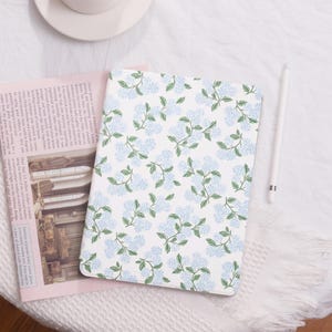 May include: A white iPad case with a blue floral pattern. The case has a subtle sheen and a soft texture.